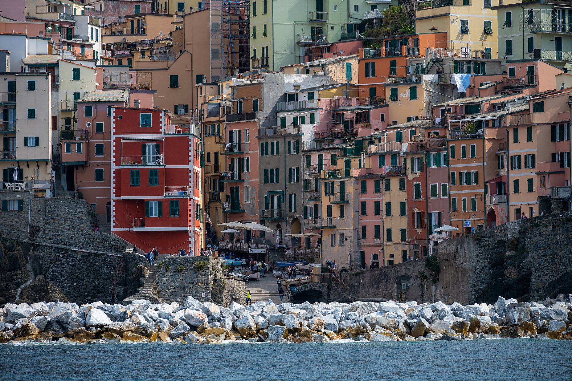 Riomaggiore Riomaggiore is het meest zuidelijke dorp. Het ligt diep ingesneden tussen de heuvels, waarop terrassen zijn aangelegd voor de landbouw. De huizen hebben de typisch Ligurische kleuren (rood, roze, oker) en leunen tegen de helling aan. Riomaggiore telt zo'n 2.000 inwoners en is daarmee met Monterosso het grootste dorp. Het dorp ontstond al in de twaalfde eeuw. Stefan Cruysberghs